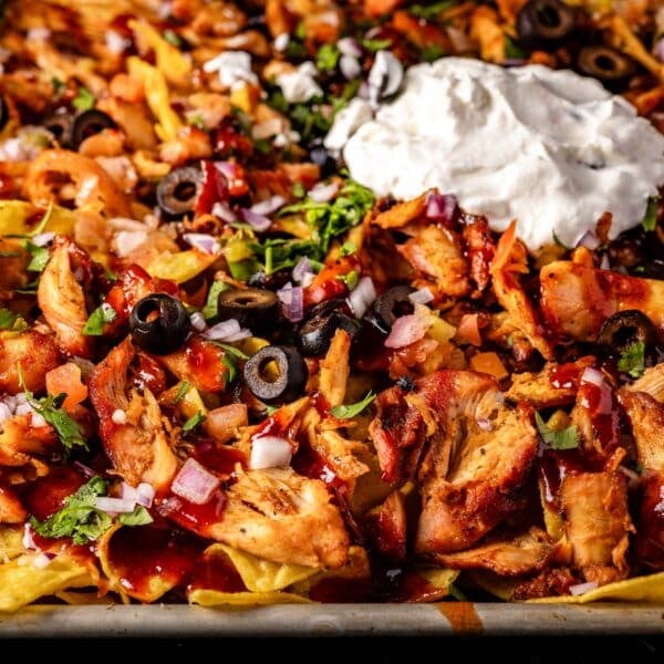 A baking sheet of tortilla chips topped with melted cheese, olives, and sour cream.