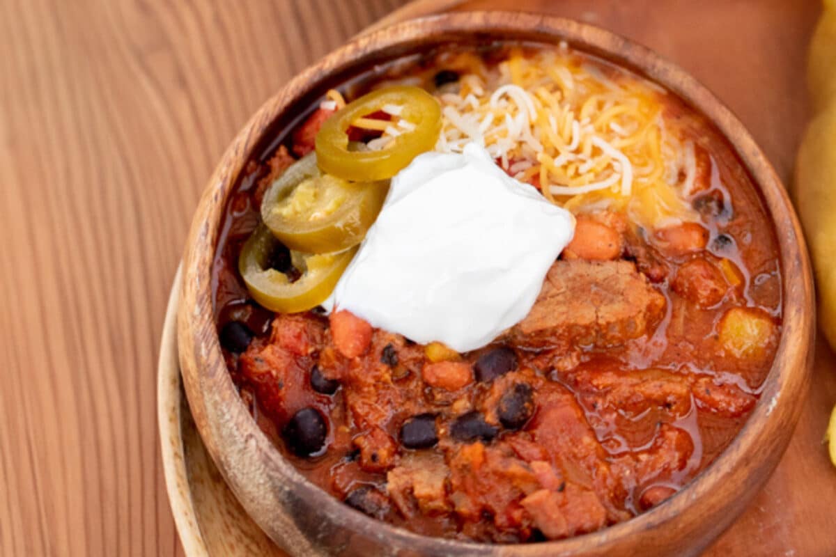 A homemade brisket chili in a wooden bowl topped with sour cream and shredded cheese.