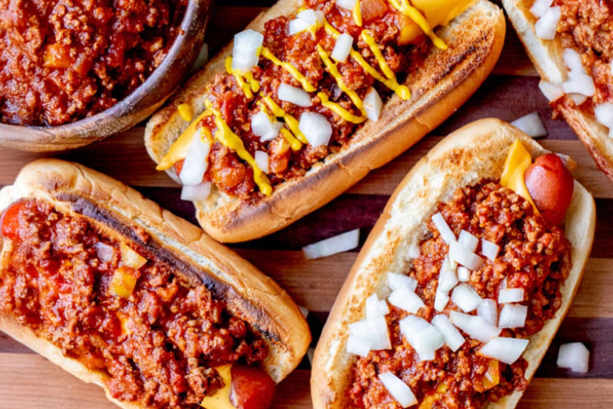 Various homemade chili dogs on a serving platter with a bowl of chili.