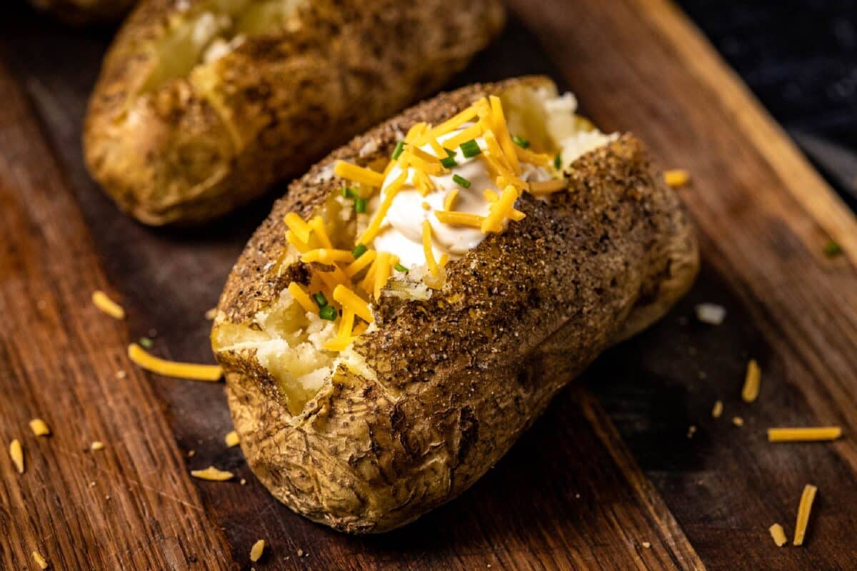 Two baked potatoes topped with cheese and sour cream on a wooden serving platter.