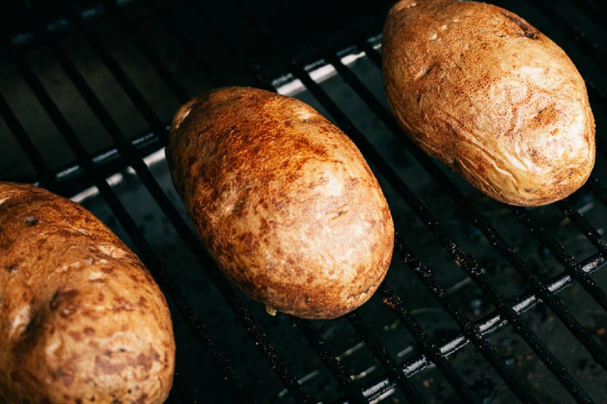 Three potatoes sitting on grill grates.