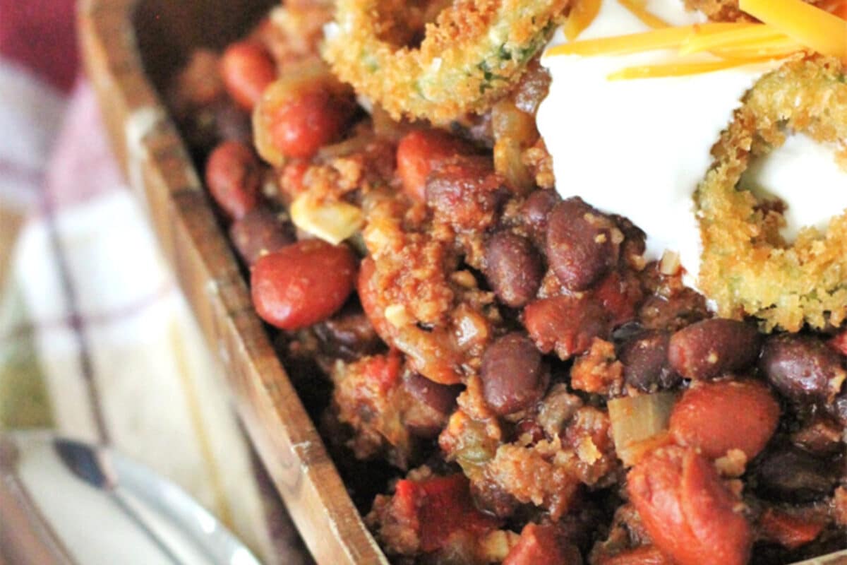 Smoked chili in a wooden bowl topped with fried jalapeño rings.