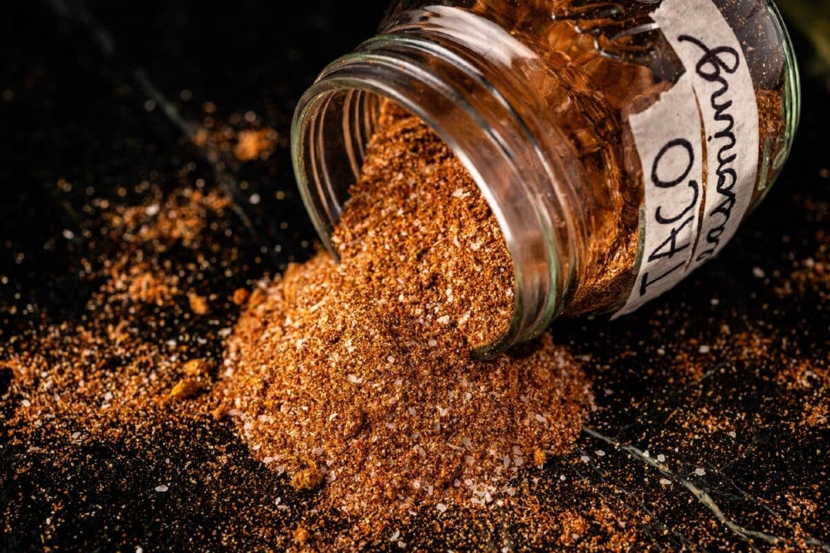 A glass jar of homemade taco seasoning spilling onto a counter.