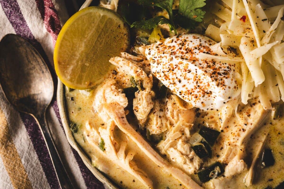 A homemade white chicken chili in a bowl next to a spoon and tablecloth.