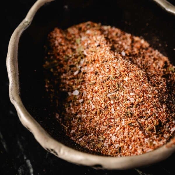 A bowl filled with creole seasoning on a black surface.