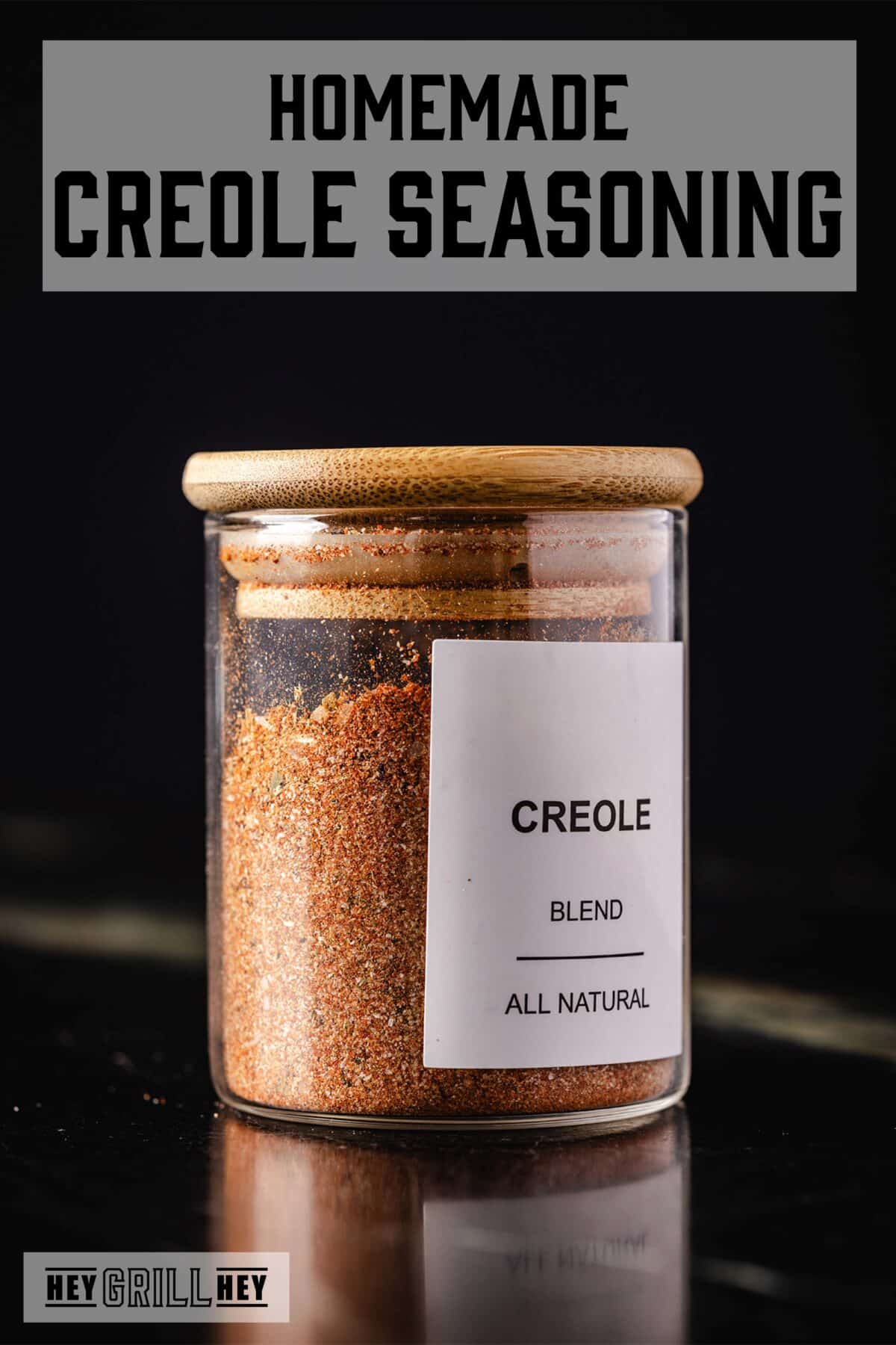 A glass jar of seasoning with a cork in it. The text overlay reads "Homemade Creole Seasoning' at the top, and "Hey Grill Hey" at the bottom.