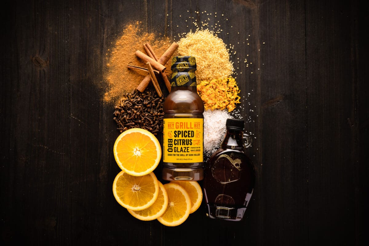 A bottle of Spiced Citrus BBQ Glaze on a table surrounded by the raw ingredients for the glaze.