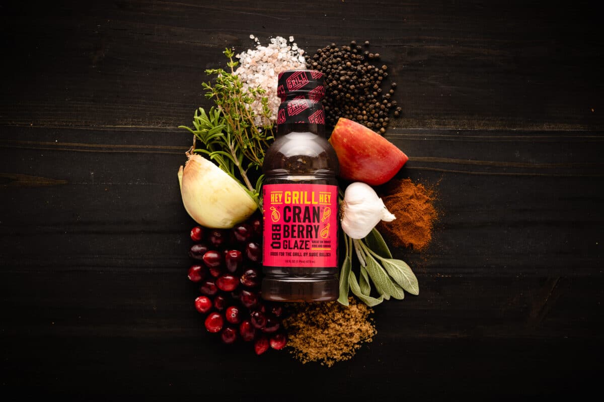 A bottle of Cranberry Glaze on a table surrounded by the raw ingredients for the glaze.