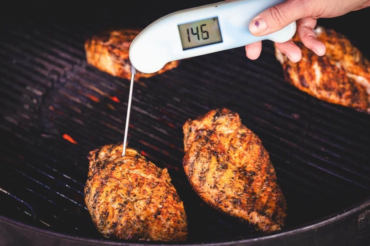 Chicken breasts being grilled, while a meat thermometer probing one of them reads 145 degrees F.