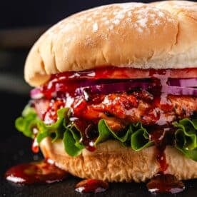 A chicken sandwich with lettuce, tomato, and onion, dripping with BBQ sauce.