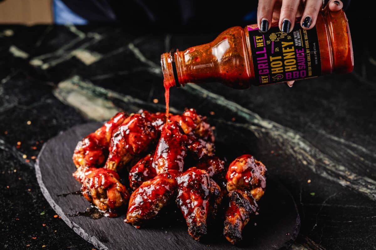 A pile of wings on a black platter and a bottle of sauce pouring onto them.