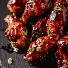 Chicken wings on a black plate coated in Hot Honey BBQ Sauce.