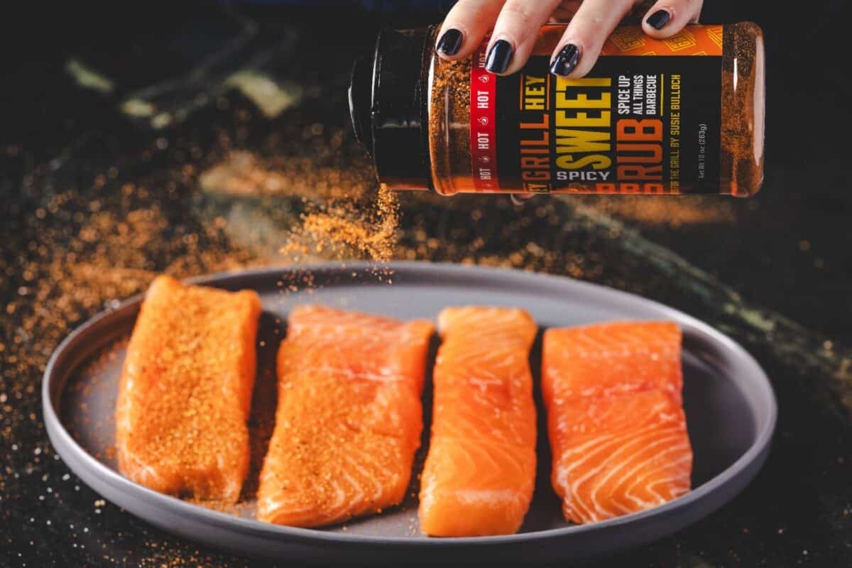 Salmon fillets on a plate being seasoned with Spicy Sweet Rub.