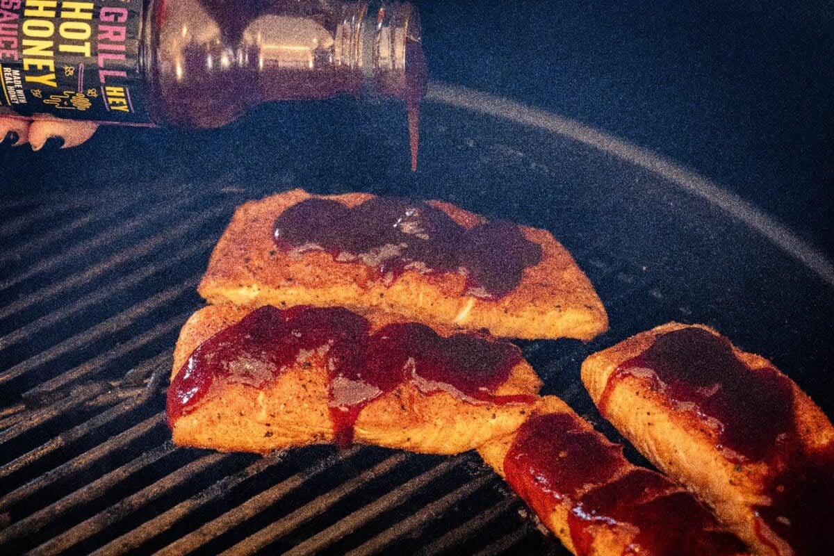 Salmon fillets on the grilled being drizzled with Hot Honey BBQ Sauce.