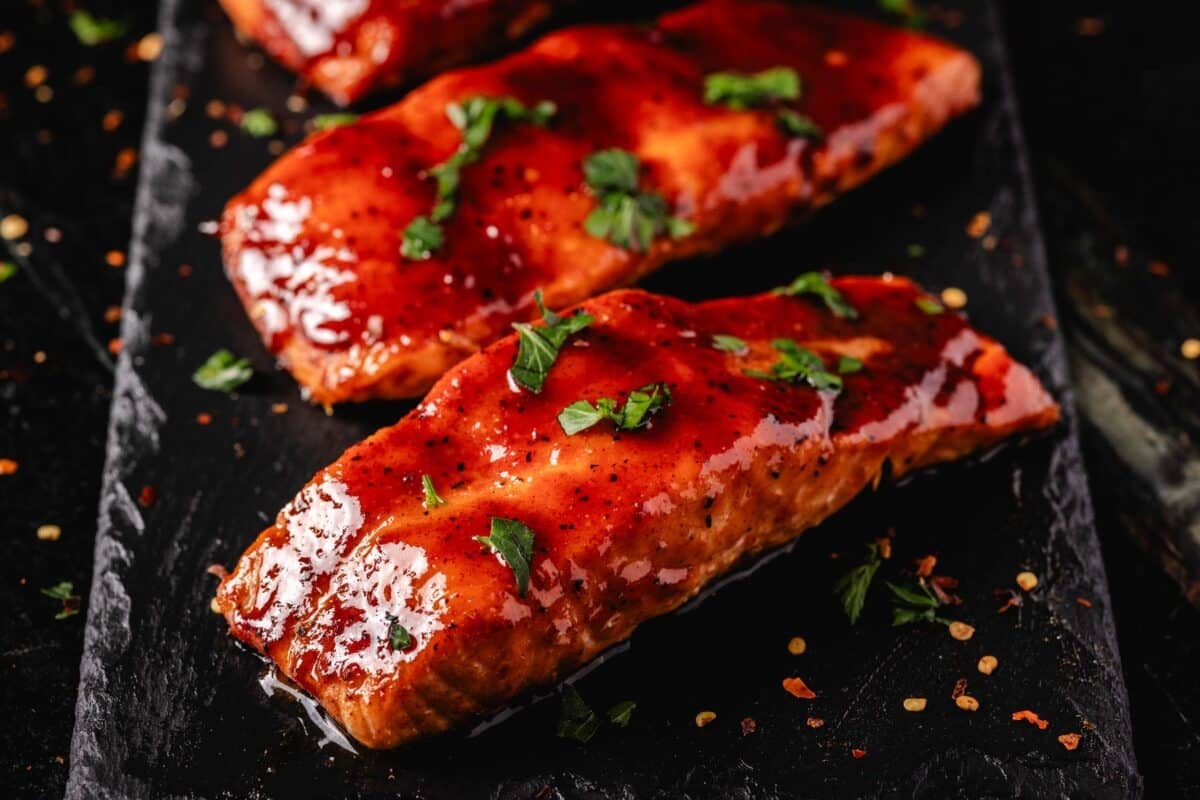 Hot Honey glazed salmon fillets on a black platter sprinkled with sliced green onion.