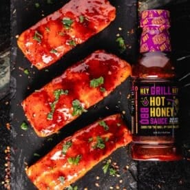 Grilled, sauced fish fillets on a black platter next to a bottle of BBQ sauce and a bottle of BBQ rub.