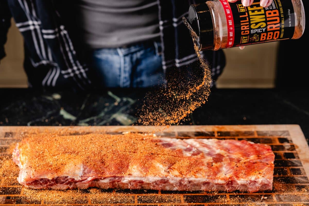 A rack of ribs on a baking sheet being sprinkled with BBQ rub.