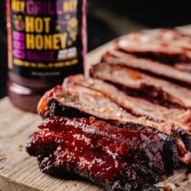 Sliced ribs on a cutting board next to a bottle of Hot Honey BBQ Sauce.