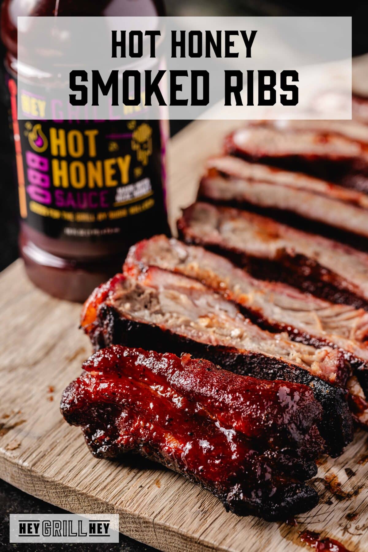 Sliced ribs on a cutting board next to a bottle of sauce. The text overlay reads "Hot Honey Smoked Ribs" at the top. and "Hey Grill Hey" at the bottom.