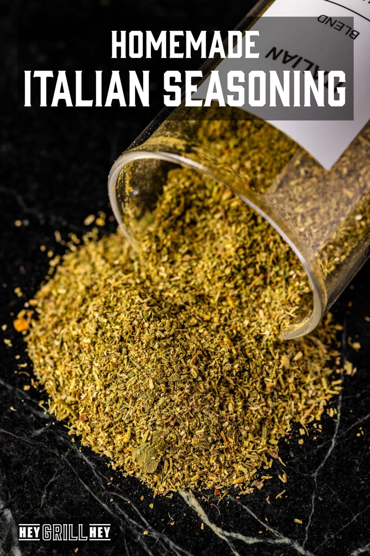 A clear glass jar of seasoning tipped over and spilling out. The text overlay reads "Homemade Italian Seasoning" at the top, and "Hey Grill Hey" at the bottom.