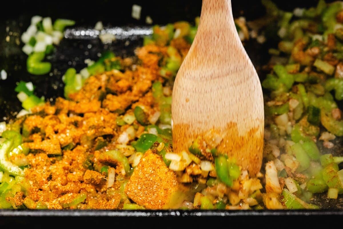 A wooden spoon stirring chicken, sausage, and veggies in a pot.