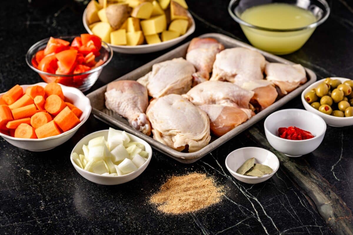 A cast iron pot of raw poultry surrounded by bowls of veggies and seasonings.