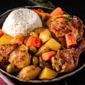 A bowl of pollo guisado chicken, carrots, potatoes, and a scoop or rice.