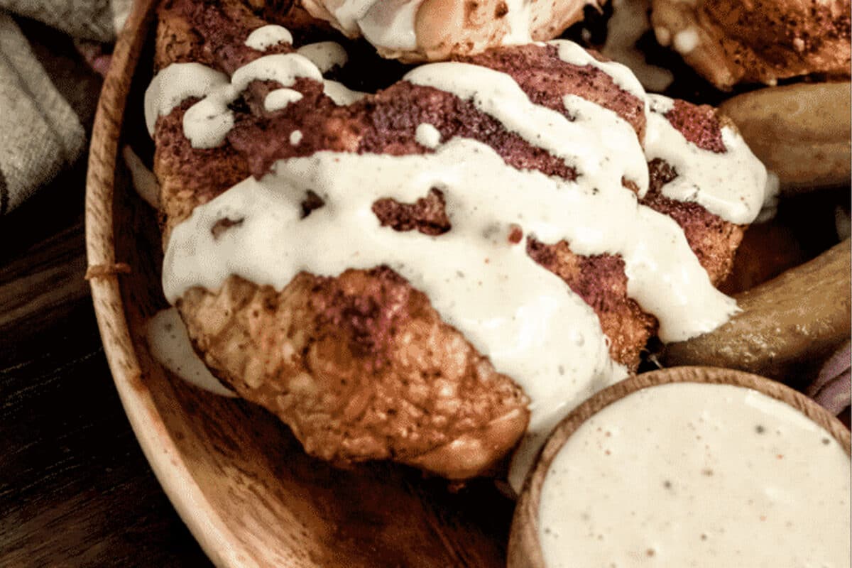 A plate of grilled chicken drizzled with Alabama white sauce, and a bowl of the sauce.