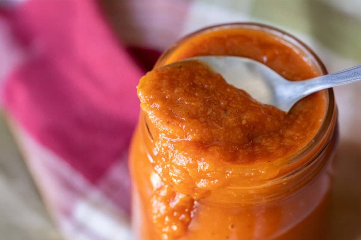 A spoon resting on a jar of sauce next to a tablecloth.