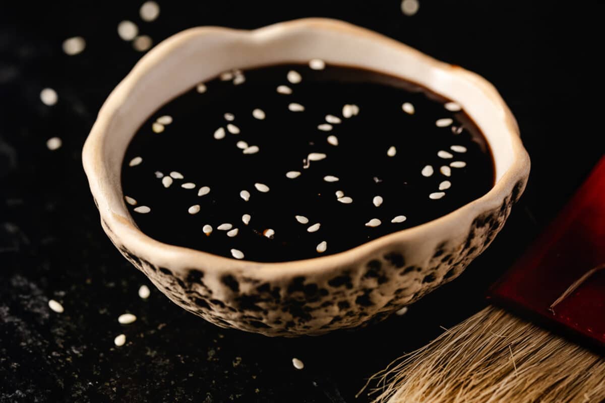 A white, speckled bowl filled with dark liquid next to a brush on a table.