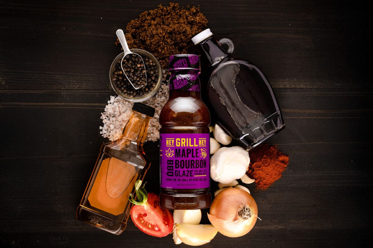 A bottle of Maple Bourbon Glaze on a table surrounded by the raw ingredients for the glaze.