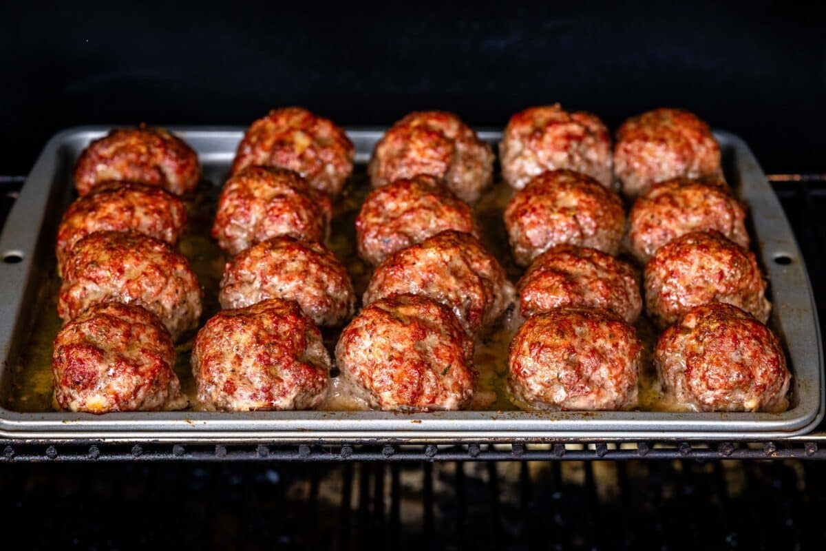 A baking sheet topped with formed ground beef on smoker grates.