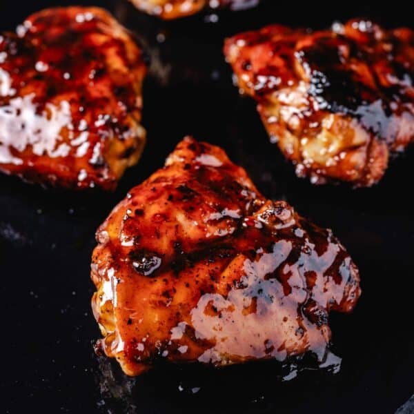 Three BBQ chicken thighs on a black platter.