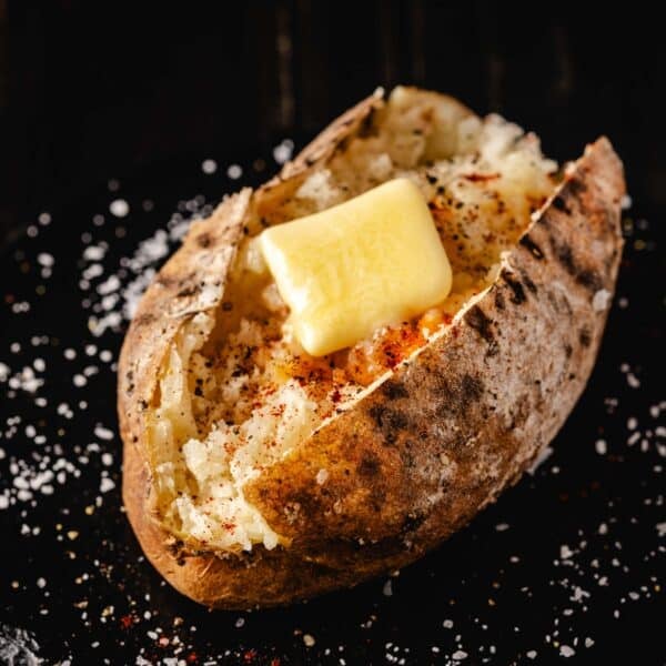 A cooked potato sliced open with a pad of butter resting on top. The surface around it is sprinkled with salt.