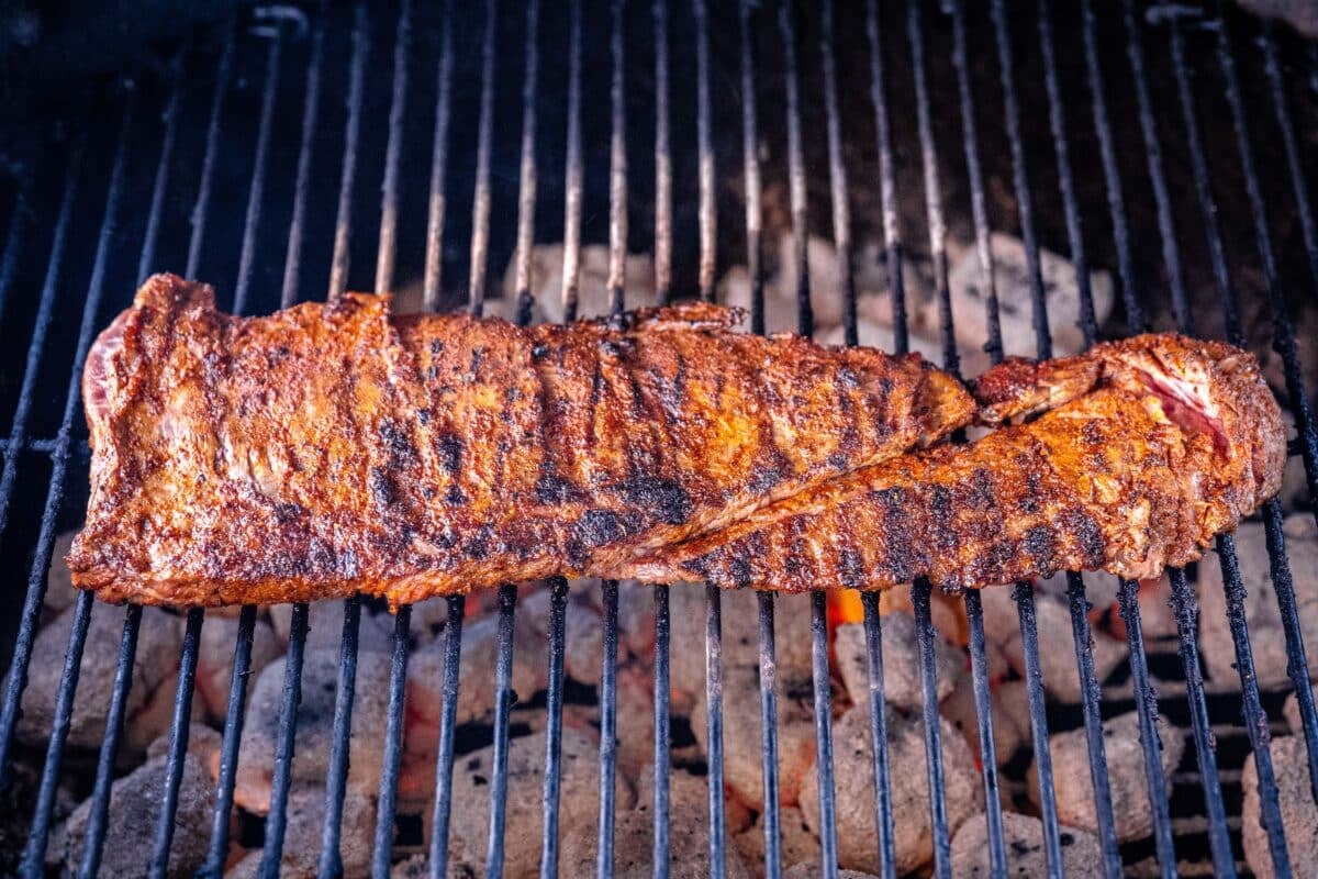 Carne asada meat on the grates of a charcoal grill.