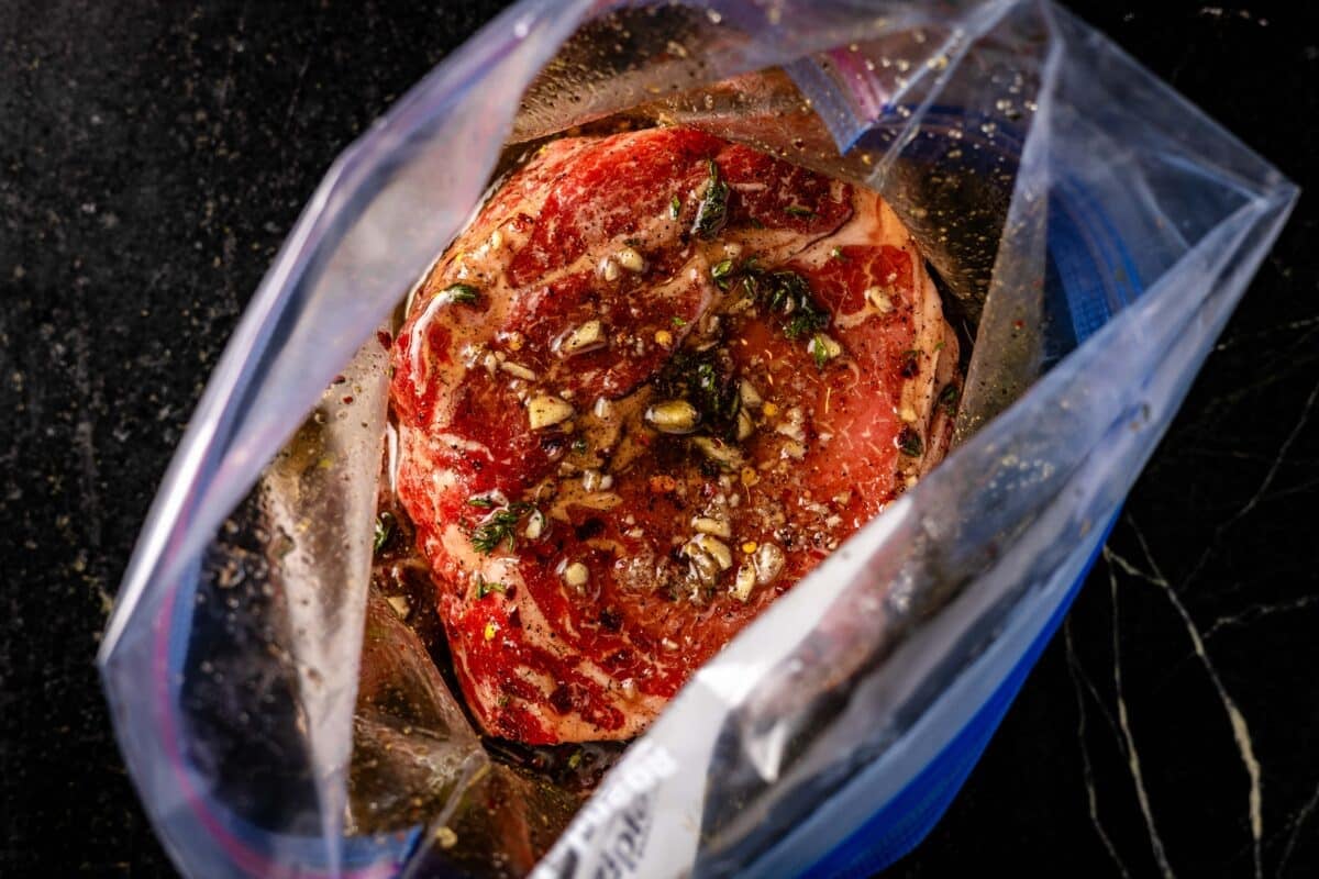 A raw steak topped with seasonings in a zip-top bag.