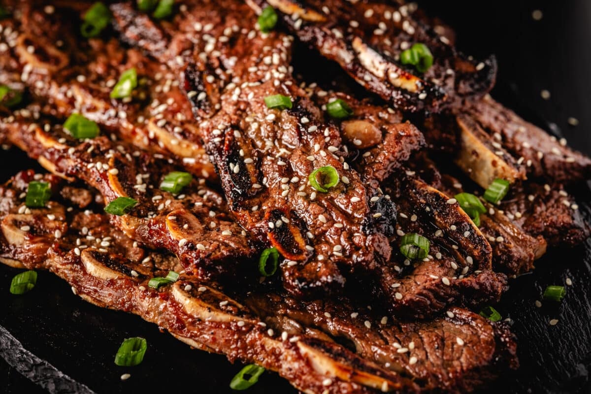 Korean BBQ beef on a black plate topped with sesame seeds and sliced green onion.