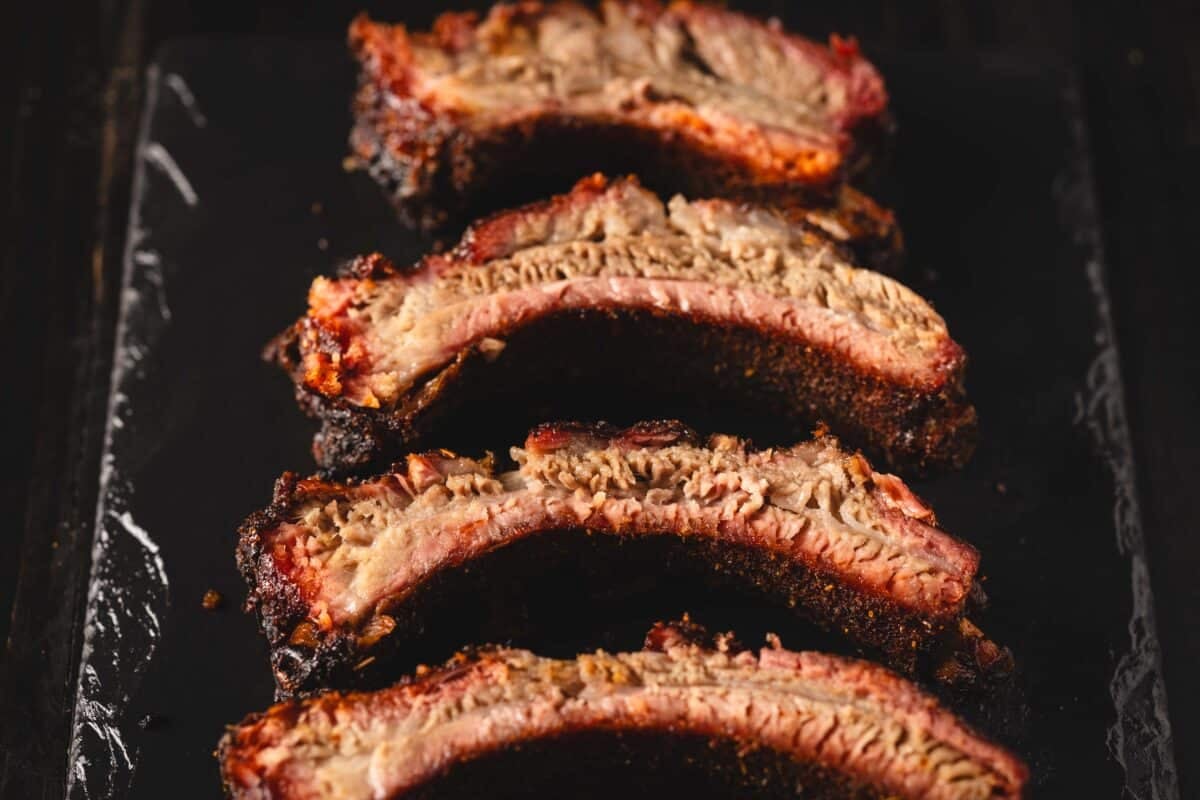 An overhead shot of sliced ribs laying on the side on a black serving platter.