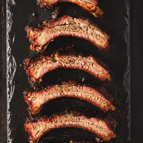 An overhead shot of sliced ribs laying on the side on a black serving platter.