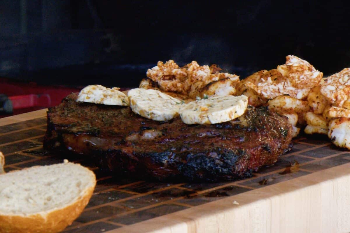 A steak resting on a cutting board with pads of compound butter melting on top of it.