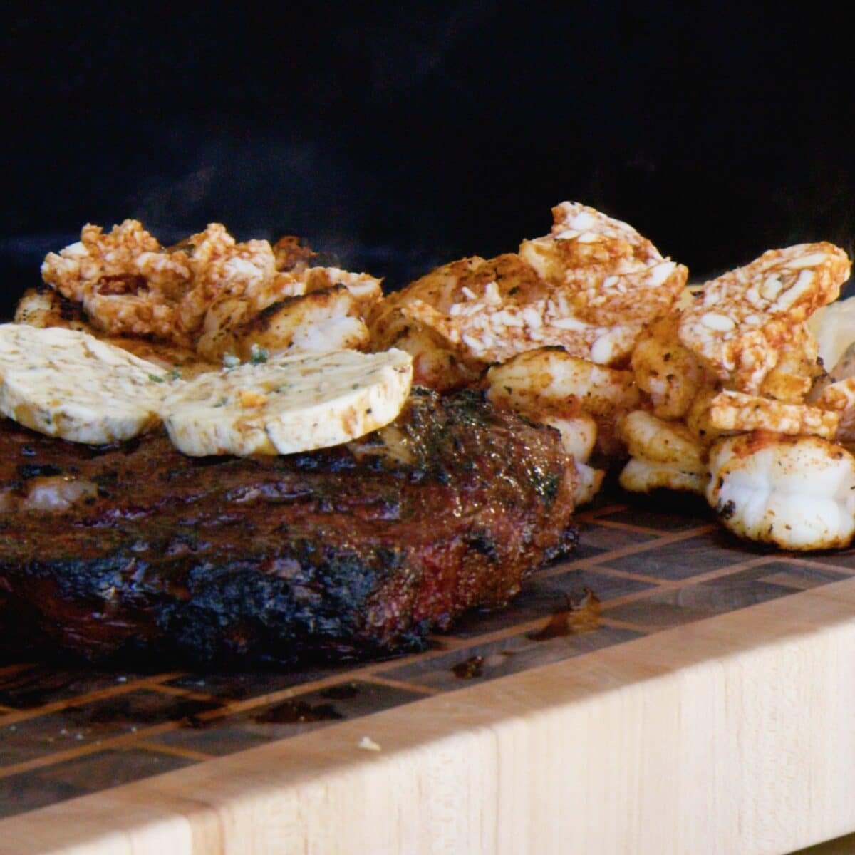 Various grilled proteins resting on a cutting board with butter pads melting on them.