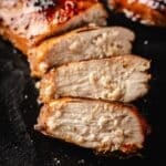 A cooked, sliced chicken breast on a black plate.