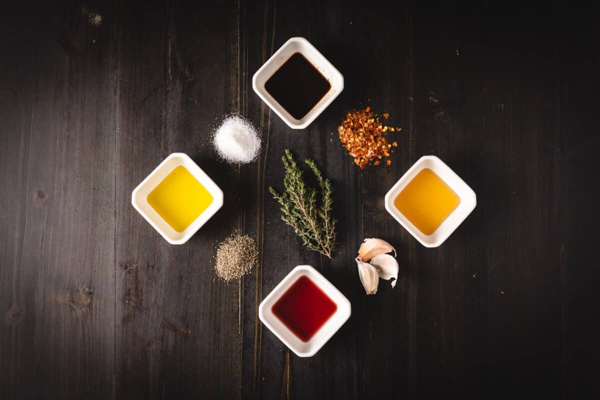 Four white bowls with liquid ingredients, surrounded by piles of loose seasoning and thyme leaves.