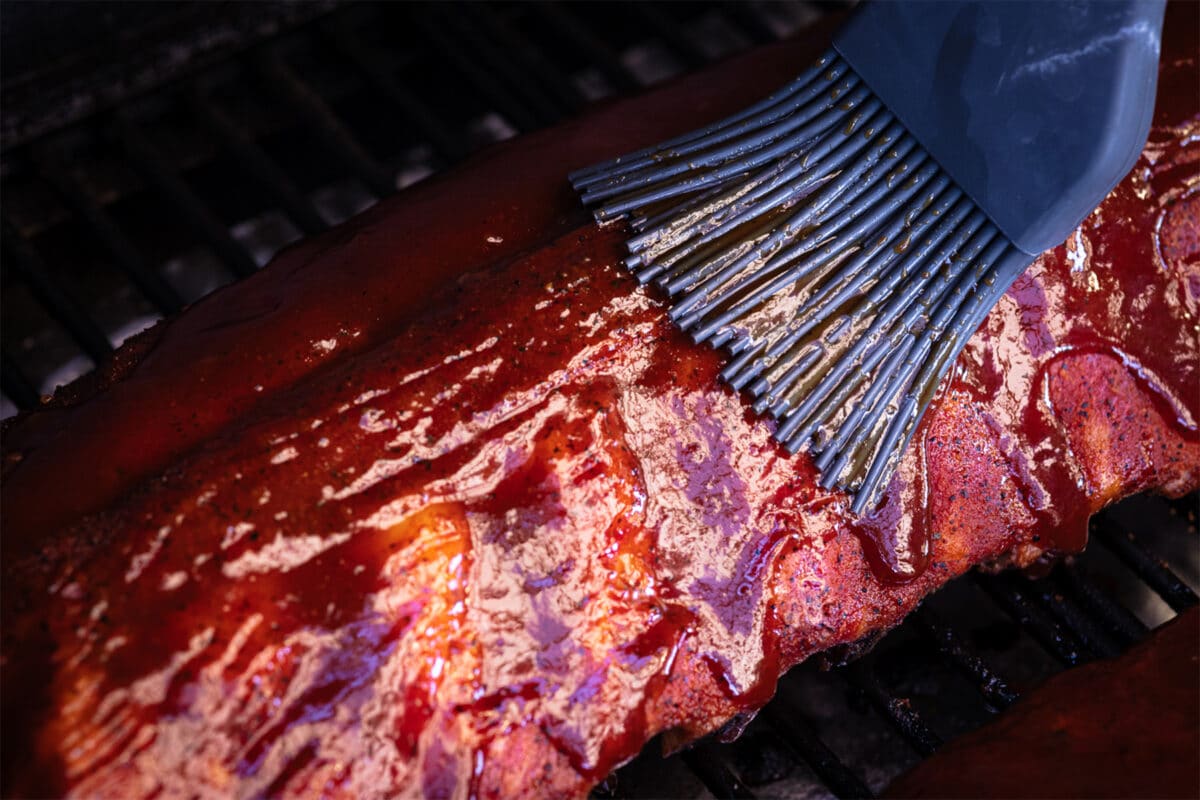 Baby back ribs on the grill being basted with bbq sauce.