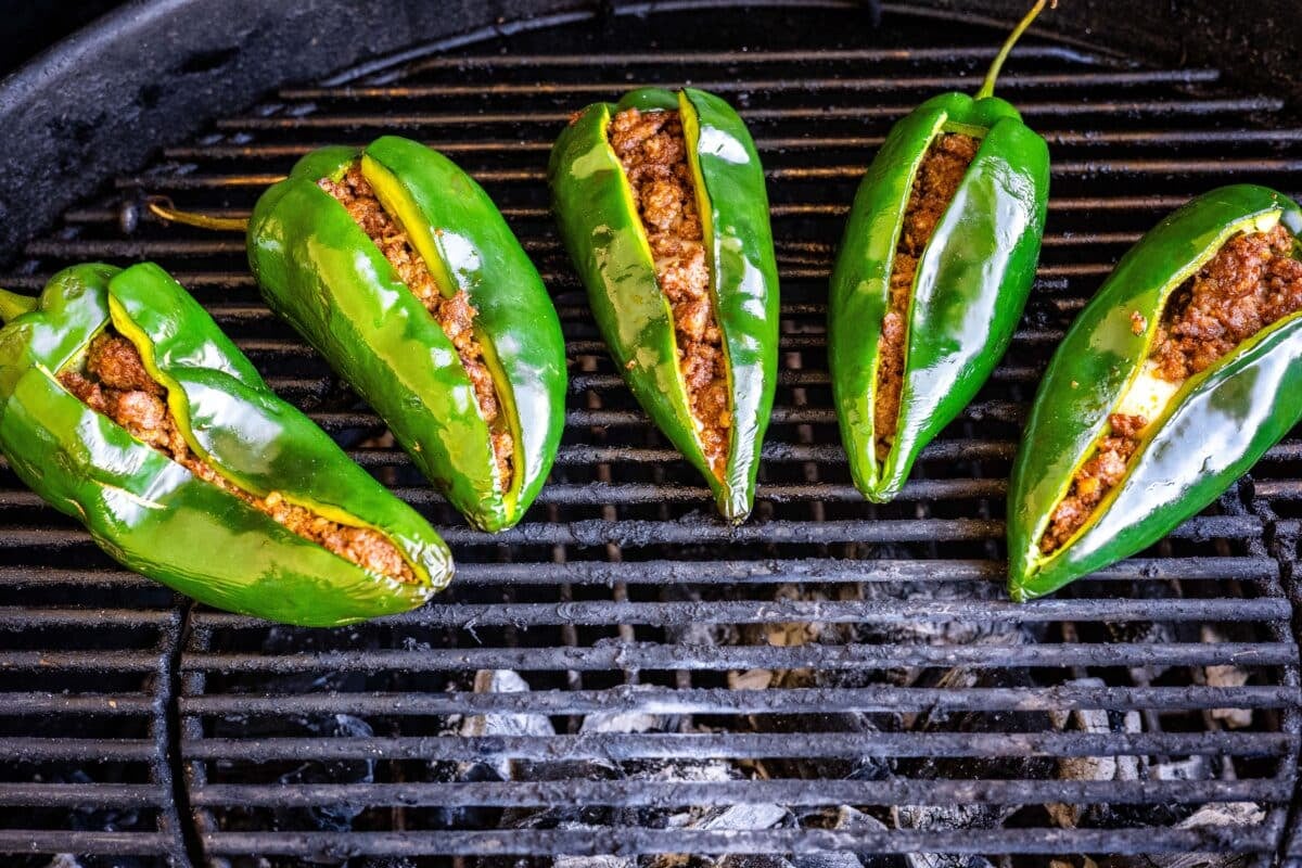 Five stuffed Chile relleno peppers being grilled over charcoal.