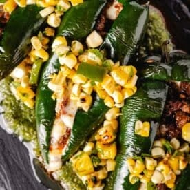Two stuffed, grilled Chile relleno peppers topped with corn salsa on a bed of salsa verde.