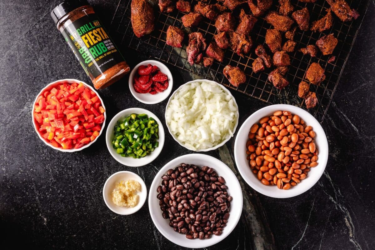 Stew meat, a bottle of BBQ rub, and several bowls with beans and diced veggies.