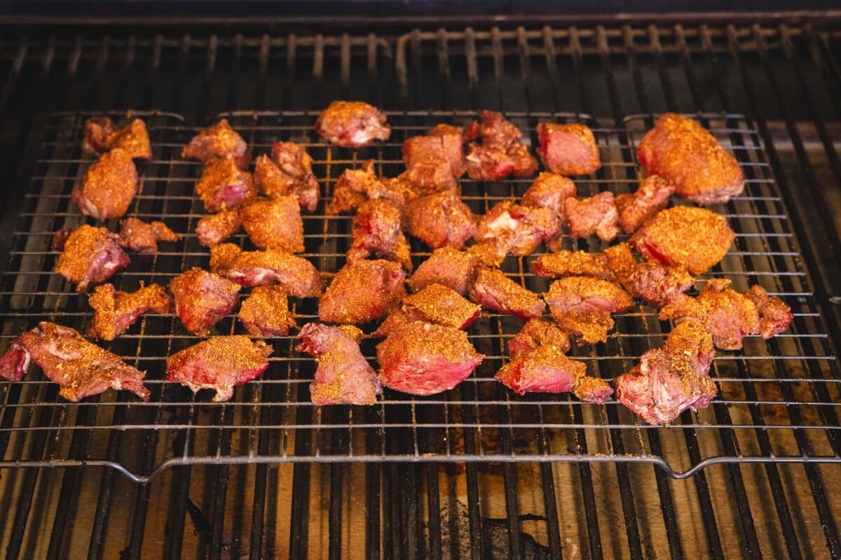 Cubed and seasoning beef on a wire rack on the smoker.