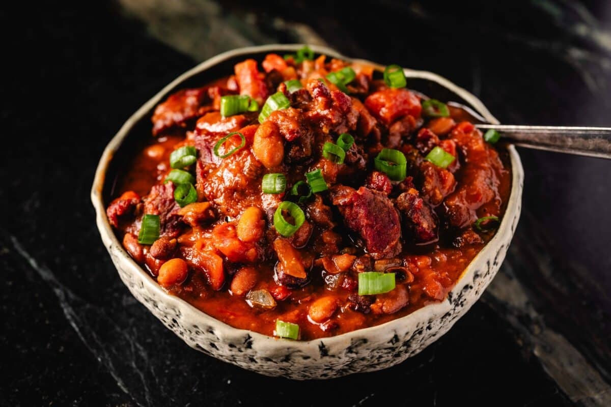 A cream-colored bowl filled with a beef chili topped with sliced green onions.