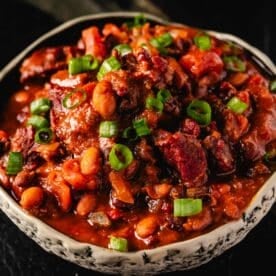 A cream-colored bowl filled with a beef and bean stew topped with sliced green onions.